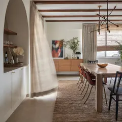 In this dining room, we used a long wooden table and exposed ceiling beams to create an earthy, rustic feel. The sheer curtain, caught in the breeze, adds a sense of movement and lightness to the space.