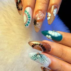 An artistic and abstract nail set with an earthy color palette. This design features a mix of patterns, including dots, fans, and floral-inspired shapes, all tied together with delicate gold bead accents.