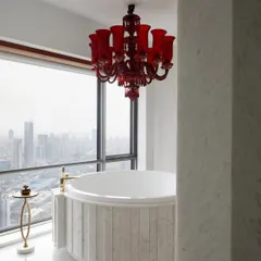 In this master bathroom high above the Mumbai skyline, luxury meets drama. A vintage red Murano glass chandelier hangs over a custom marble spa bath, creating a romantic and intensely personal retreat with an unparalleled view of the city.
