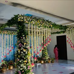 A wide view of an indoor stage with a Pichwai-style backdrop and lush floral pillars.
