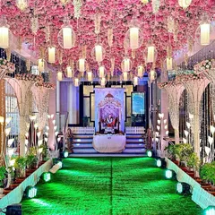 This pretty entrance features a ceiling of pink cherry blossoms and hanging lanterns. The walkway is flanked by large crystal and pearl decorative pieces, lit from below to create a soft, elegant glow. This design is ideal for a classy night function like a reception or Sangeet.