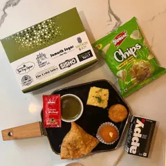 This customized snack box includes a samosa, dhokla, a savory mini kachori, and a ladoo for a sweet finish. It's accompanied by a pack of chips and a drink, making it a complete and satisfying snack for any event.