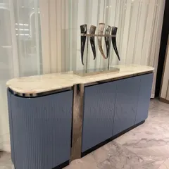 A beautiful custom console with a white marble top and a unique base combining stainless steel and fluted blue-grey panels. The interior is lined with a surprise pop of orange leather.