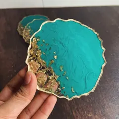 A close-up of a teal and gold coaster, showing the intricate swirls in the resin and the texture of the gold flakes.