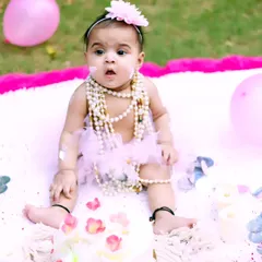 A look of surprise and delight during an outdoor cake smash. Her pearl necklaces and tutu add a touch of glamour to the messy fun.