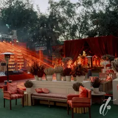 An outdoor lounge area designed for a quintessential Delhi wedding, using a rich palette of reds and oranges. The stage is set with dramatic lighting, while the seating area is adorned with dried floral arrangements in earthy tones.