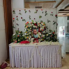 A floral tribute arrangement for a memorial service. A photograph is placed within a wreath of fresh flowers including lilies, carnations, and roses.
