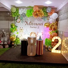 This complete jungle theme setup for a second birthday includes a custom backdrop, extensive balloon work, themed pedestals for the cake, and a large light-up number '2' for a fantastic photo zone.