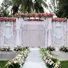An ethereal wedding entrance designed to look like a pristine white temple gate, adorned with delicate pink and white florals. I create settings that feel like they are straight out of a fairytale.