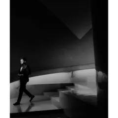 A dramatic black and white shot of the groom, Shrey, walking down a modern staircase. The architectural lines and strong contrast create a powerful and cinematic portrait.