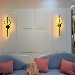 A close-up of the details that bring a living room to life. This image shows modern, minimalist wall sconces installed on a wall with subtle, curved molding, perfectly complementing the soft blue sofa and pink cushions.
