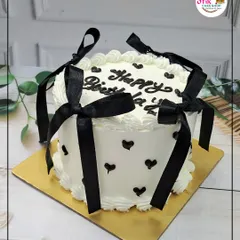 A chic black and white birthday cake. The white buttercream is decorated with little black hearts and tied with elegant black ribbons for a modern and stylish look.
