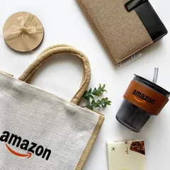 A flat-lay of an eco-friendly gift set for Amazon. It showcases a branded jute tote bag, a glass tumbler with a branded sleeve, and a jute-cover notebook, all reflecting the brand's identity.