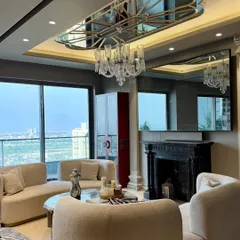 A wider view of the Gulshan Dynasty living room, showcasing the spacious layout, the elegant crystal chandelier, and the expansive windows that flood the space with natural light.