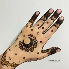 A bold Eid design with a large crescent moon surrounded by a leafy wreath. The hand is covered in a delicate pattern of dots and flowers.