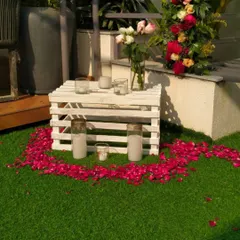 A close-up of the romantic decor, featuring a heart made of rose petals on the grass, surrounded by candles in glass holders.