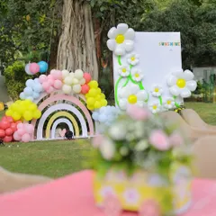 A beautiful shot of the sunshine party setup, with a themed floral centerpiece in the foreground and the main rainbow and daisy backdrop in the background, showing the depth of the decor.