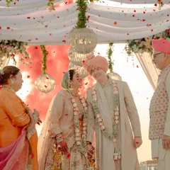 Pure joy and celebration under the mandap. The couple shares a laugh as confetti and smoke fill the air, surrounded by their happy family.