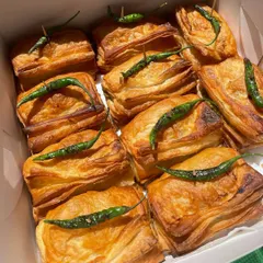 A box full of my crispy, flaky, and freshly baked Vada Pav Puffs. Each puff is topped with a fried green chili for that authentic touch. A Jain option is also available.