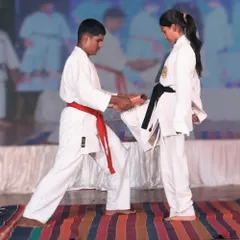 Our dojo fosters a spirit of mutual growth, where senior students help train the next generation. This image shows a male student assisting a female karateka in a power breaking drill, highlighting our supportive community.