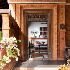 A threshold is a sacred space. Here at the Varadarajan House, an antique carved wooden door frame, set within earthy laterite walls, marks the passage from the lush outdoors to the calm interior, celebrating our rich cultural heritage.