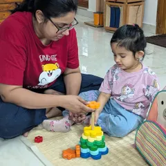 A mother and daughter work together on a colorful flower stacking toy. This shared activity during the settling-in period makes the new environment feel safe and familiar.