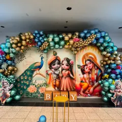 Celebrate your baby's arrival with a traditional Krishna-themed ceremony. This vibrant setup features beautiful illustrations of Lord Krishna and Yashoda, a magnificent peacock, and a grand balloon arch in metallic blues and golds, perfect for a Seemant Sanskar or naming ceremony.