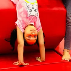 The pure joy of accomplishment. This close-up captures a young student's proud smile as she holds a handstand against a tumbler, a moment that perfectly represents the confidence boost our classes provide.
