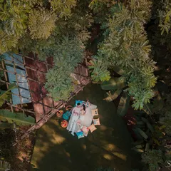 A bird's-eye view of a perfect afternoon. This drone shot captures a couple enjoying a romantic picnic, nestled in a clearing surrounded by lush greenery, creating a feeling of a private, hidden paradise.