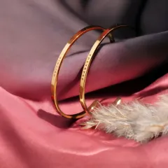 Two gold-plated cuff bracelets, engraved with 'HRITHIK' and 'AKANKSHA', displayed on soft fabric. This set is ready to be gifted to a special couple.