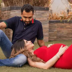 An outdoor session capturing a relaxed and intimate moment, with the mom-to-be resting her head on her partner's lap on a beautiful green lawn.