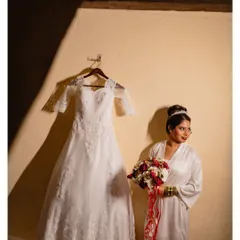 An artistic shot of the bride in her robe, standing next to her wedding dress. The dramatic lighting adds a touch of mood and anticipation.