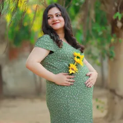 A beautiful solo portrait in a casual green dress, adorned with sunflowers. The warm sunlight highlights the mother-to-be's happy glow.