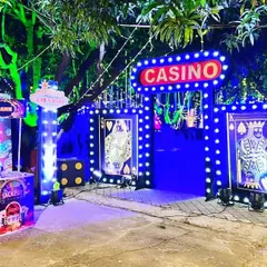 We can transform any outdoor space for a party. Here is a full casino theme entrance we built, featuring a lit-up "Casino" marquee sign, custom gates with playing card designs, and a "Bank" booth for activities.