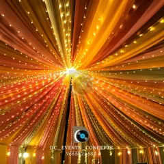 Another example of our ceiling decor, this time with warm-toned fabrics and string lights creating a spectacular sunburst effect for an indoor event.
