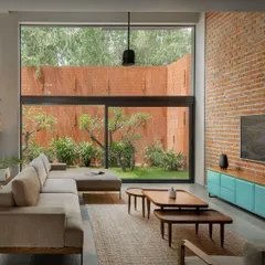 A view of the living room, where the neutral sofa and jute rug are contrasted by a pop of turquoise in the console. The exposed brick wall adds warmth and texture, while the large window frames the garden like a living piece of art.