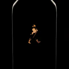 Walking in the dark. This minimalist shot of Johnnie Walker uses only edge lighting to trace the iconic bottle's silhouette. The focus is entirely on the striding man logo, which appears to float in the darkness, creating a powerful and mysterious image.