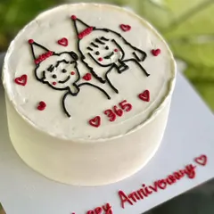 A sweet and simple anniversary cake featuring a cute stick-figure illustration of the couple, complete with party hats and hearts to mark 365 days together.