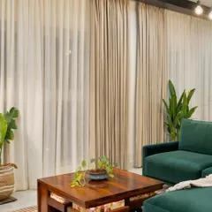 A closer look at the industrial-chic living space we designed. The combination of an emerald green sofa, warm wood coffee table, and sheer curtains creates a perfect balance of raw textures and refined comfort.