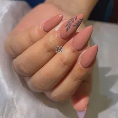 A chic and minimalist design featuring a matte nude polish with a simple, hand-painted black leaf accent.