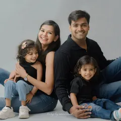 A relaxed and joyful family of four, dressed in casual jeans and black tops, smiling warmly for the camera in a clean, simple studio setting that emphasizes their connection.