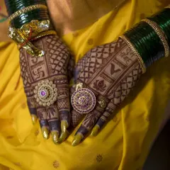 A close-up of the bride's hands, showcasing her stunningly intricate mehendi, beautiful rings, and traditional green bangles.