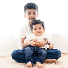 A gentle and loving portrait of two brothers. The older brother sits with his arm around the younger one, showcasing his protective and caring nature.