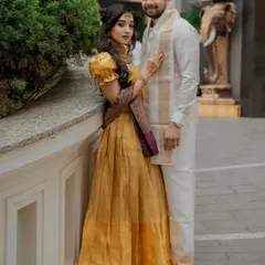 The couple together, showcasing a coordinated look for their event. The bride's golden gown is complemented by the groom's traditional white and gold attire.