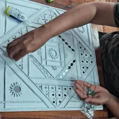 A student carefully places mirrors onto the wet clay of her Lippan art panel. This tactile process is both meditative and rewarding, resulting in a unique piece of home decor.