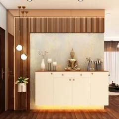 A minimalist pooja unit featuring a simple console with a Buddha statue. The backdrop of fluted wood paneling adds warmth and texture, creating a calm and understated spiritual corner.