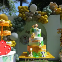 This photo shows a full dessert setup for a child's first birthday party. I created a three-tiered jungle animal themed cake as the centerpiece, complemented by matching cupcakes displayed on a stand.