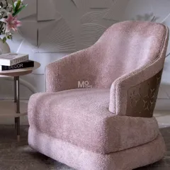 The Blush Haven Armchair embodies modern elegance with its plush blush bouclé fabric. The design is elevated by a precision-cut metal detail in antique brass, inspired by architectural jaalis, that wraps around the backrest.