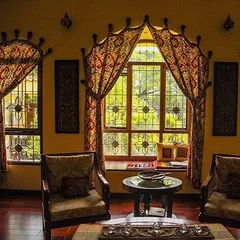 This cozy seating area in the Roopa Hariprasad Residence features a bay window with custom traditional drapery. The space is designed to be a comfortable nook for reading and conversation, filled with warm light and rich textiles.