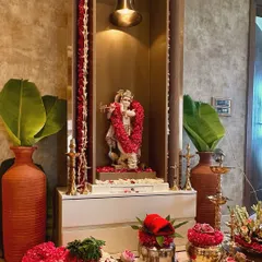 A home mandir decorated for a housewarming puja. We adorned the Krishna idol with a fresh rose garland and surrounded it with traditional elements like banana leaves, brass lamps, and bowls of flowers.